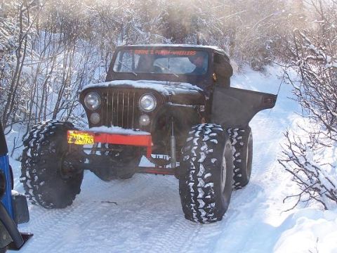 2003 Jeep TJ - A Jeep CJ-5 navigates a snowy trail with oversized tires, partially obscured by snow and winter foliage.