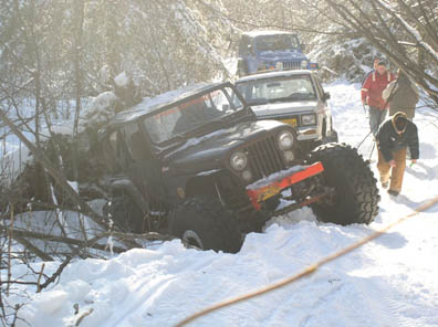 2003 Jeep TJ - A group of off-roaders attempt to free a Jeep CJ-7 that has become stuck in deep snow next to a fallen tree.