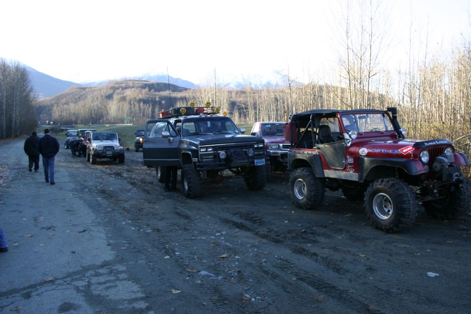 Several off-road vehicles lined up on a dirt road with trees and mountains in the background