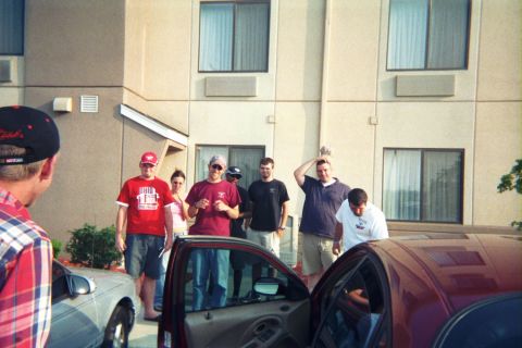 1998 Ford Taurus - A group of people gather around two sedans parked in front of a hotel.