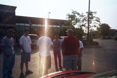 1998 Ford Taurus - A group of people are gathered in a parking lot on a sunny day.