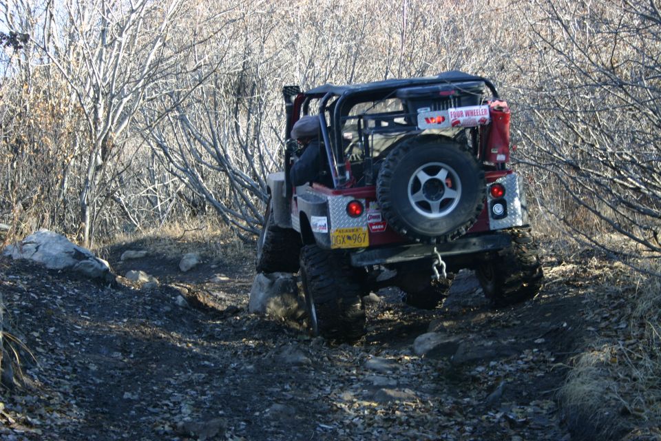 Red 2003 Jeep TJ with a spare tire on the back, navigating a rocky off-road trail