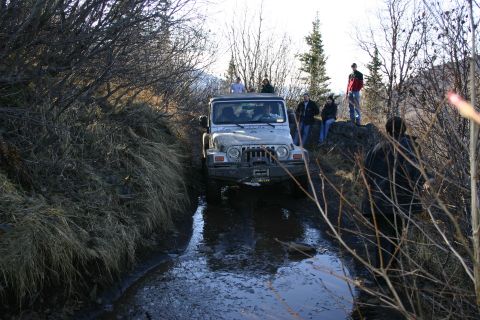 2003 Jeep TJ - A 2003 Jeep TJ navigates a challenging muddy path with onlookers observing the off-road excursion.