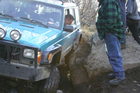 2003 Jeep TJ - A teal Jeep Cherokee XJ maneuvers through a challenging muddy terrain with onlookers present.