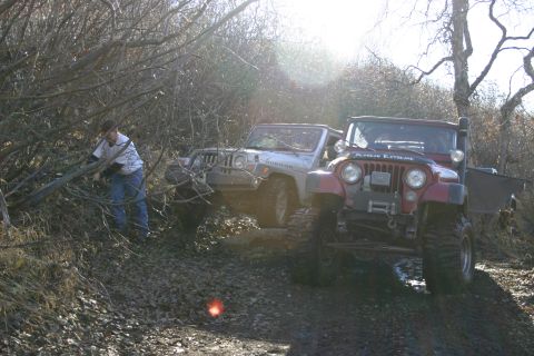 2003 Jeep TJ - Two Jeep TJs navigate a muddy, wooded trail, one with "ALASKAN EXTREME" visible on its hood.