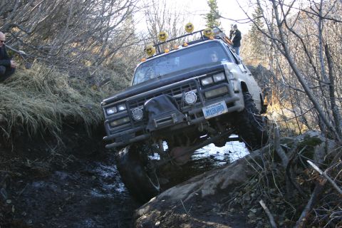 2003 Jeep TJ - This modified truck is shown off-roading on a challenging, uneven terrain with dense vegetation.