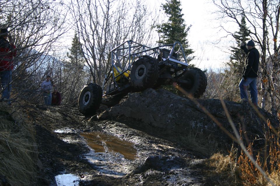 Custom buggy with roll cage climbing over a rock on a muddy trail