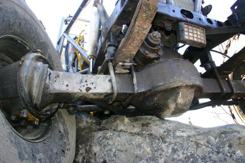 2003 Jeep TJ - Rear axle and suspension components of an off-road vehicle are visible, with the tire on rocks.