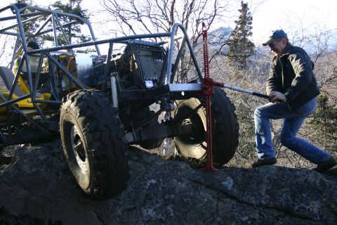 2003 Jeep TJ - A man operates a high-lift jack to free a heavily modified off-road vehicle from a rocky obstacle.