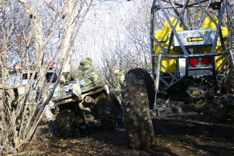 2003 Jeep TJ - Two off-road vehicles navigate a muddy, wooded terrain with one vehicle equipped with a yellow tank and a Husky toolbox.