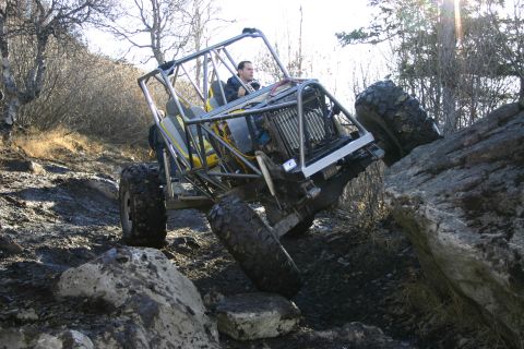 2003 Jeep TJ - A custom-built off-road buggy navigates a rocky incline, its extreme suspension and large tires.