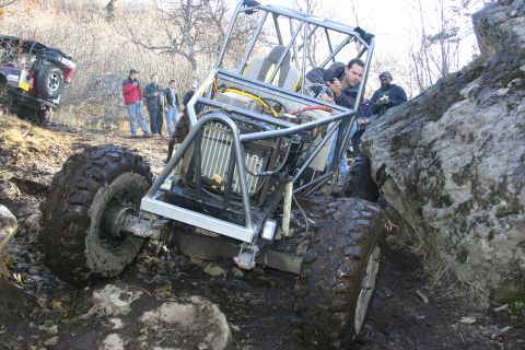 2003 Jeep TJ - An off-road buggy with a prominent roll cage and exposed engine navigates a rocky, muddy terrain, with another vehicle visible in the backg…
