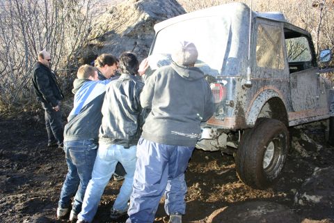 2003 Jeep TJ - A group of people push a muddy 2003 Jeep TJ out of a difficult off-road situation.