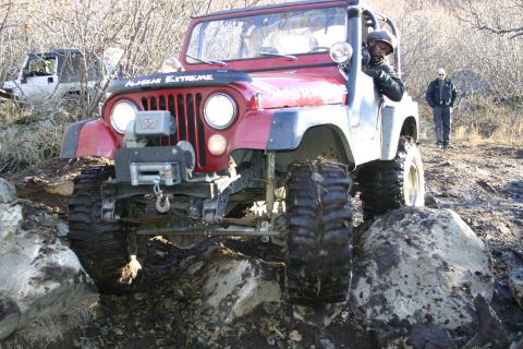 2003 Jeep TJ - A red Jeep CJ-7 navigates a rocky trail, with another vehicle visible in the background.