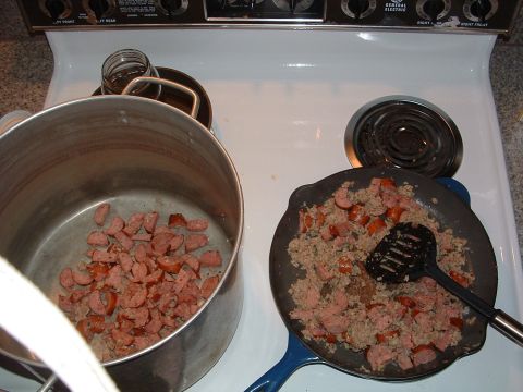 1993 Ford Bronco - Sausage and ground meat are being cooked on a stovetop in a pot and a cast iron skillet.