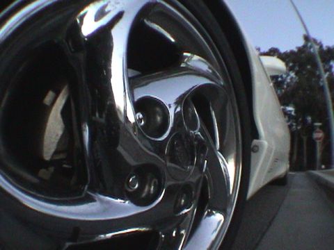 1997 Ford Probe - A close-up of a car's chrome wheel and white fender, with trees and a stop sign visible in the background.