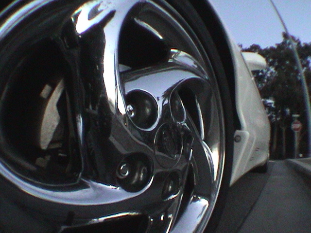 Chrome five-spoke wheel and white fender of a car, close-up view