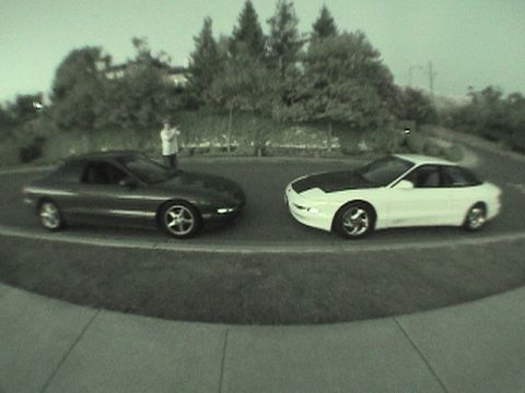 1997 Ford Probe - Two 1997 Ford Probes are seen parked next to each other on a road, with a person standing between them.