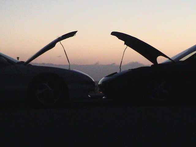two cars facing each other with hoods open at sunset