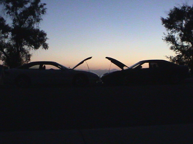 Two dark coupes with hoods open face each other at dusk