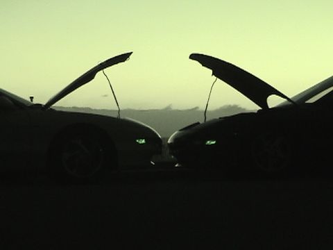 1997 Ford Probe - Two cars are silhouetted against a hazy sky with their hoods open, facing each other.