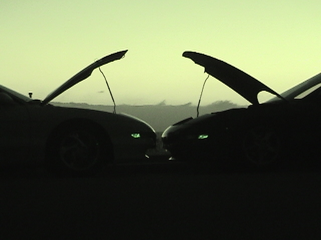 Two dark cars with hoods open face each other at dusk