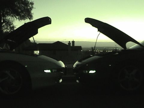 1997 Ford Probe - Two cars parked facing each other with their hoods open at twilight.