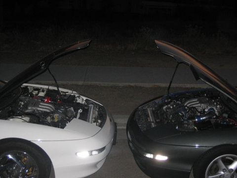 1997 Ford Probe - Two cars are parked at night with their hoods open, revealing their engines.