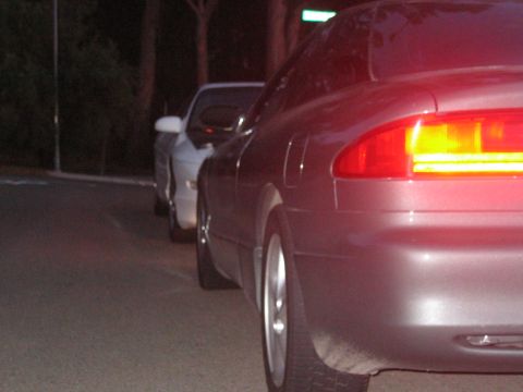 1997 Ford Probe - Two cars are parked on a street at night, with the rear of a dark coupe in the foreground.