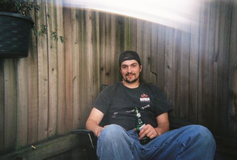 1990 Ford Bronco - A man relaxes outdoors with a beer, seated in a chair against a wooden fence.