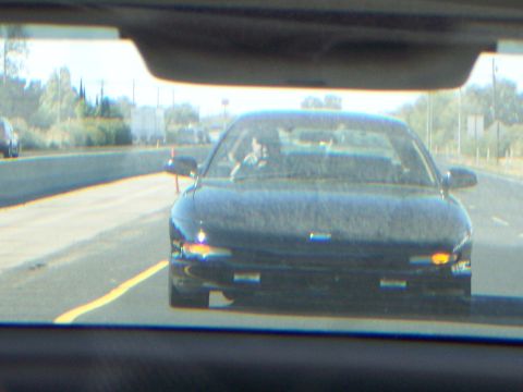 1993 Ford Probe - A black sedan is captured from inside another car while driving on a highway during the day.