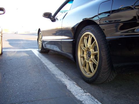 1993 Ford Probe - A black 1993 Ford Probe is parked next to another vehicle, showing its side profile and distinctive gold wheels.