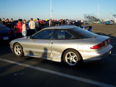 1993 Ford Probe - A silver 1993 Ford Probe is parked in a lot with other vehicles and people milling about.
