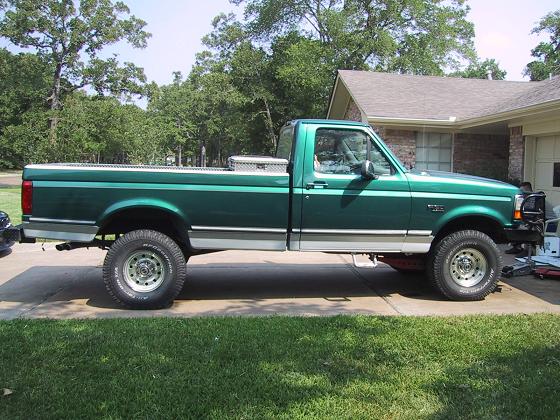 Green pickup truck parked in driveway, side view. Has a toolbox in the bed