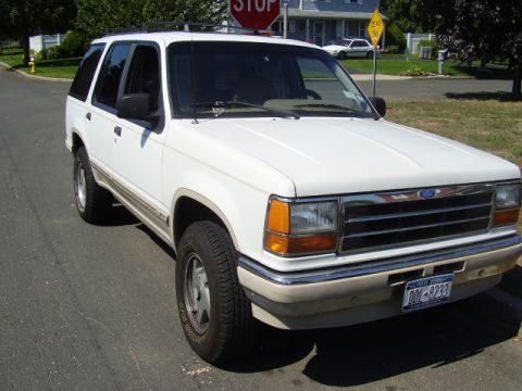 1991 Ford Explorer - A white 1991 Ford Explorer is parked on a street in front of houses.