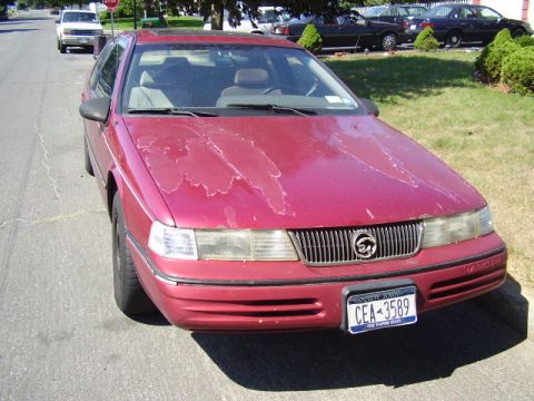 1991 Ford Explorer - A red 1991 Mercury Cougar is parked on the street, showing significant paint damage on its hood.