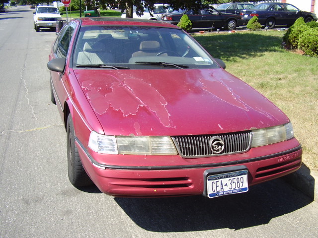 Red 1991 Mercury Cougar with peeling paint on the hood, parked on a street