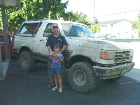 1988 Ford Bronco - Mud-covered 1988 Ford Bronco with a man and child posing for a photo.