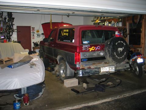 1995 Ford Bronco - The rear of a red Ford Bronco is visible, parked in a garage with a motorcycle and other items.