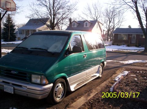 1994 Ford Aerostar - A green van with a two-tone paint job is parked on the side of the road on a cold day.