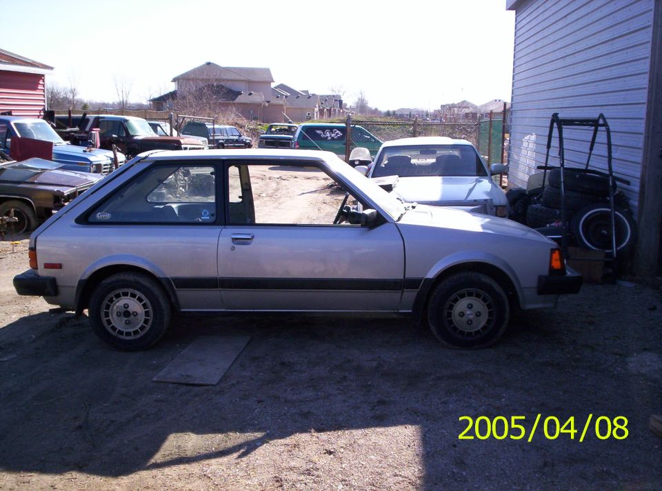Silver two-door hatchback shown in side profile on a gravel lot.