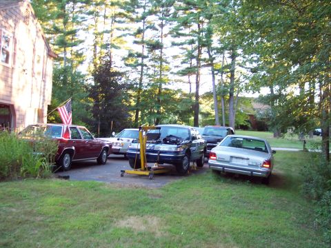 2001 Ford Crown Victoria - Several vehicles are parked in a driveway, including a 2001 Ford Crown Victoria with its engine out, suggesting repair work.