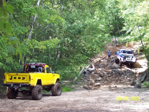 1977 Ford F-150 - Two pickup trucks navigate a challenging rocky trail in a wooded area.