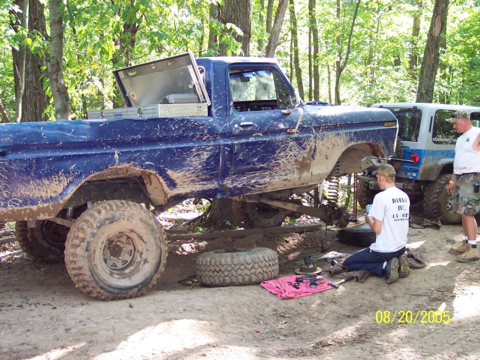 Blue 1977 Ford F-150 with lifted suspension and off-road tires, being worked on outdoors