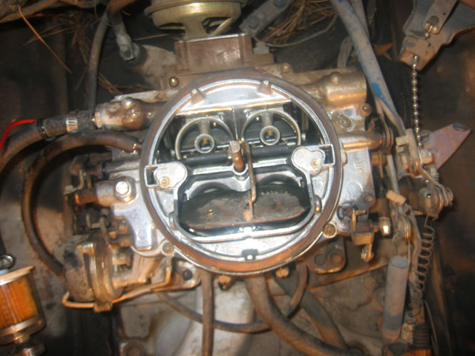 Close-up of a vehicle's carburetor with visible linkages and hoses