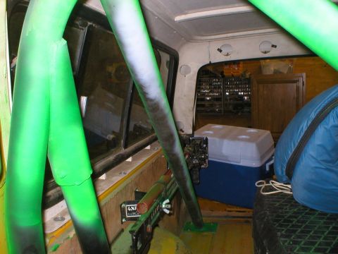 1978 Ford Bronco - Vehicle interior with a prominent green roll cage, cooler, and sleeping bag visible.