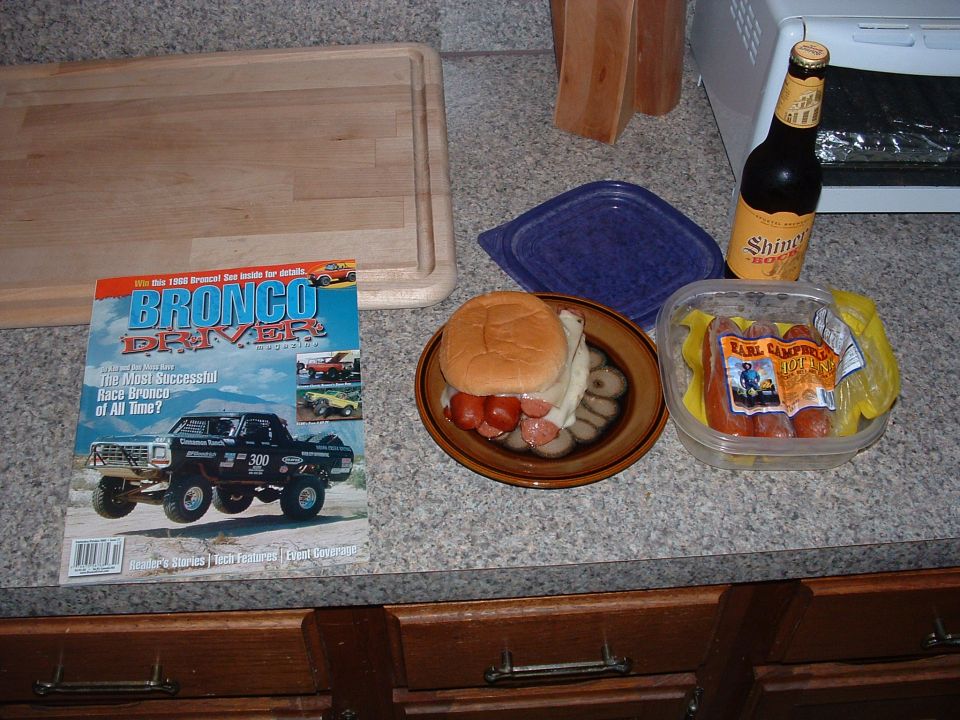 Bronco Driver magazine on counter with sandwich, sausage, and beer