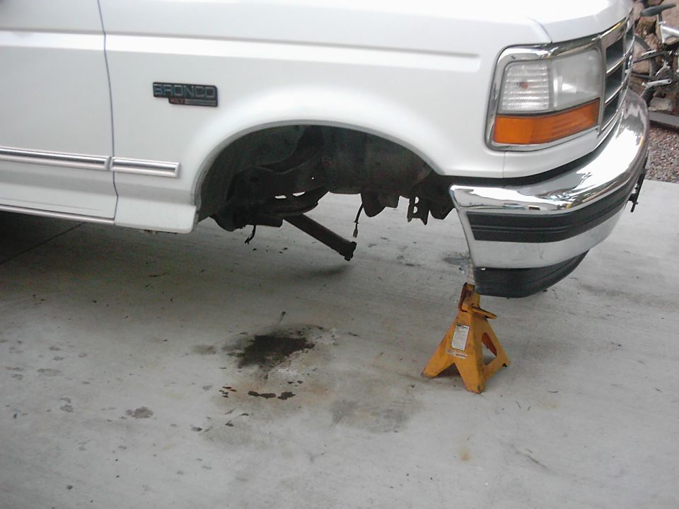 White Ford Bronco front end on jack stands, showing exposed suspension and chrome bumper