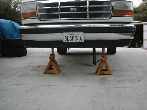 1978 Ford Bronco - Front view of a white Ford truck, possibly a Bronco, raised on jack stands for maintenance.