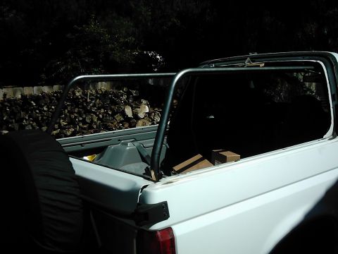 1978 Ford Bronco - Rear view of a white SUV with a roll cage and a spare tire. Firewood is piled behind the vehicle.